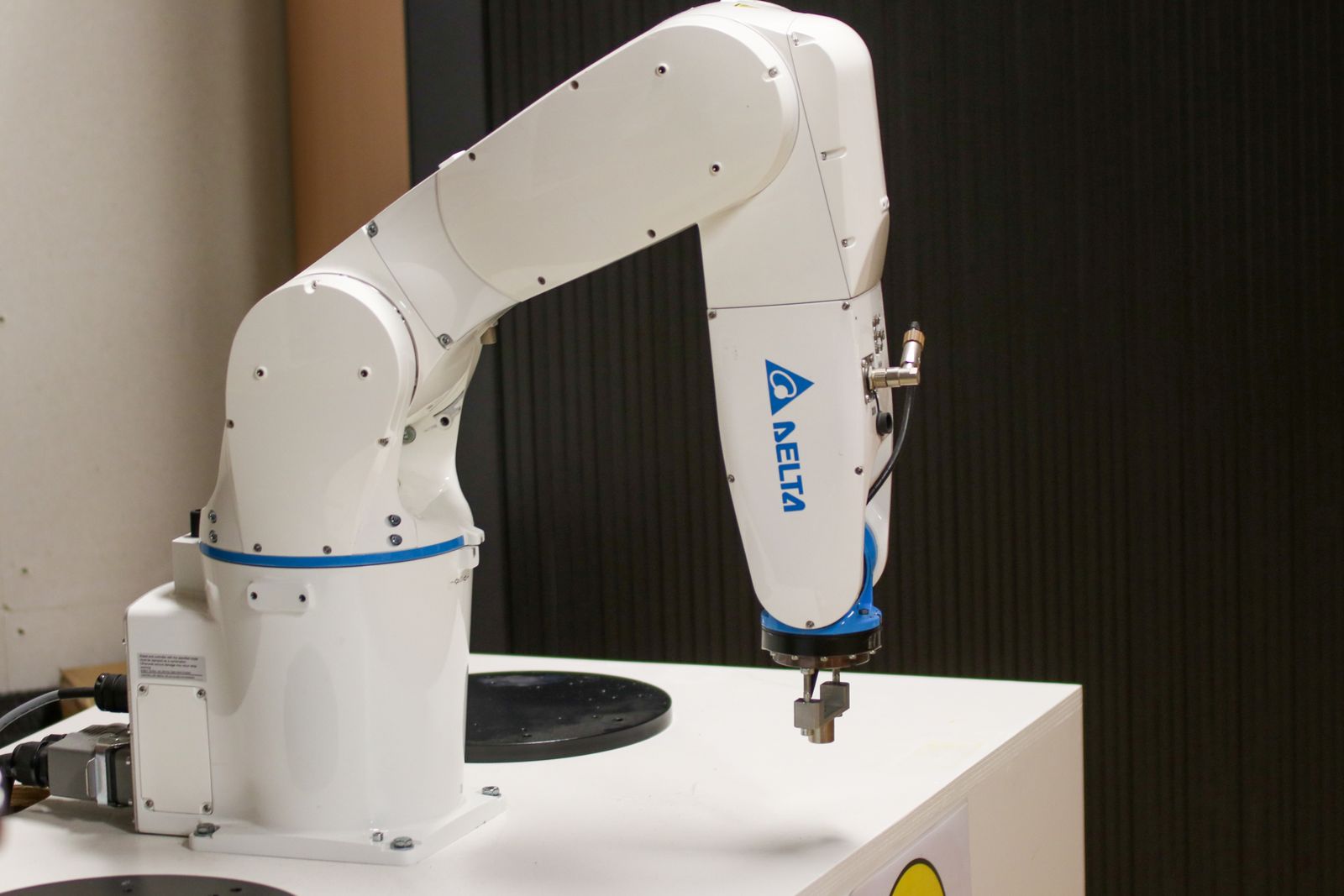 White and blue robot arm with a small gripper mounted on a display table.